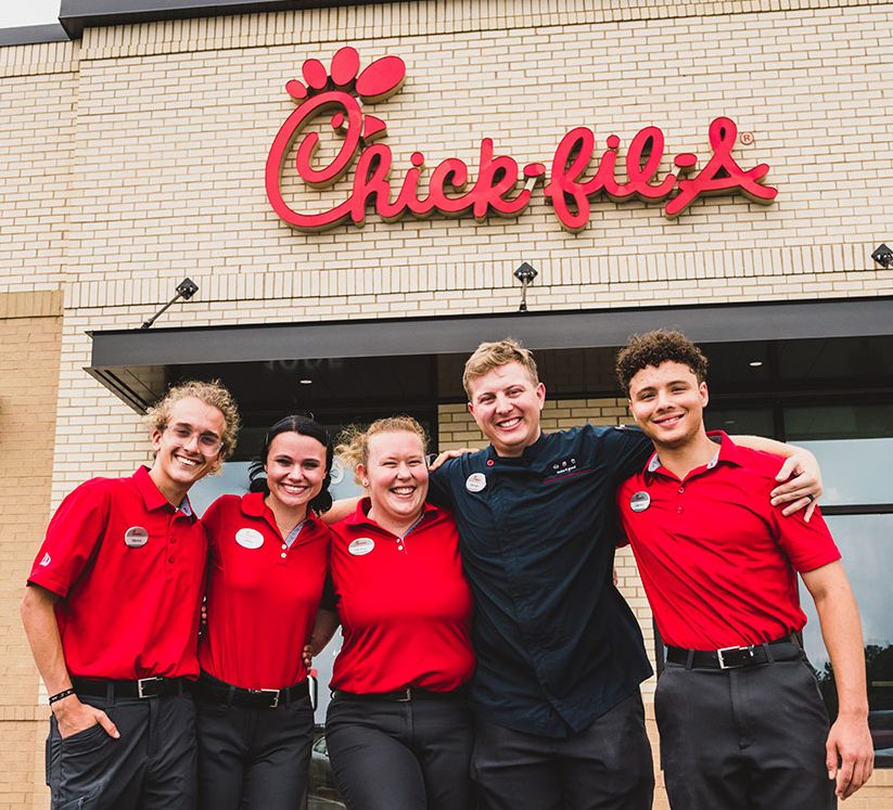 Chick‑fil‑A Team Members smiling together outside of a Chick‑fil‑A restaurant.