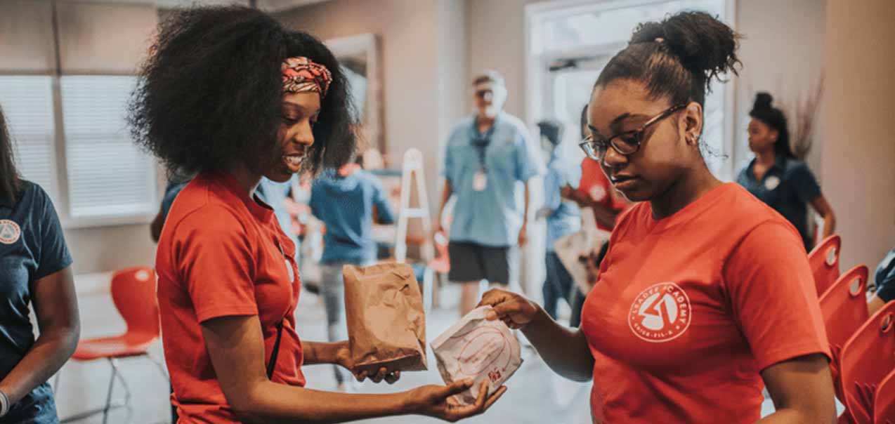 Two girls wearing Leader Academy holding food to be donated.