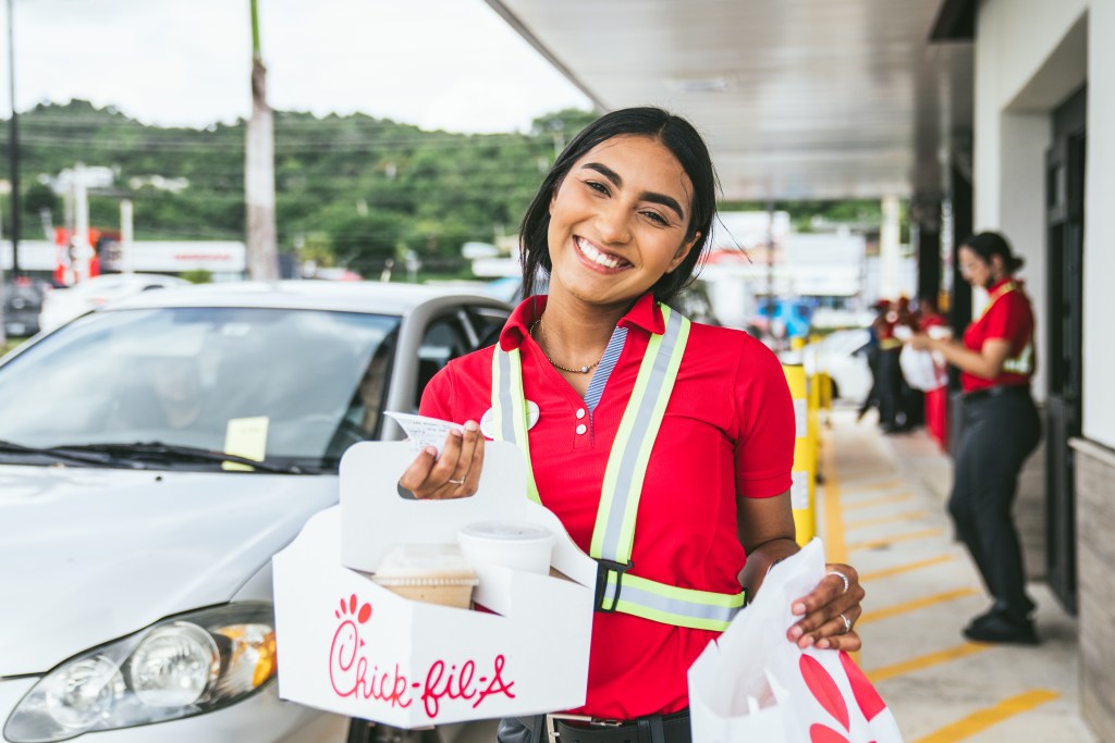 A smiling Chick-fil-A Team Member holding food and beverages in the drive-thru.